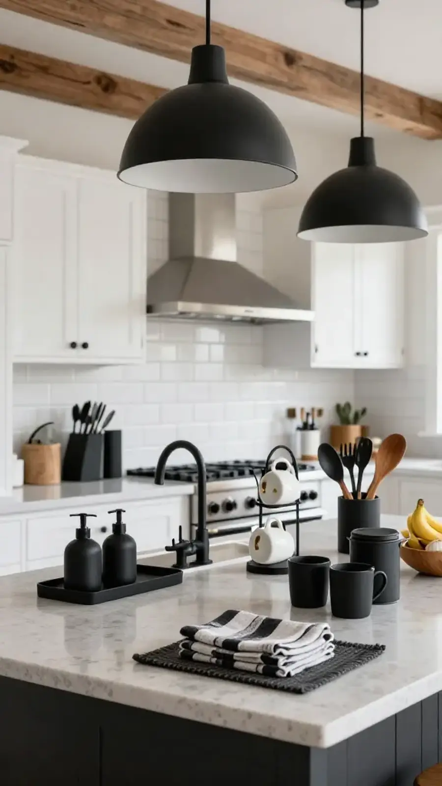 Modern white kitchen with a gray island styled with matte-black decor accessories, including soap dispensers, knife block, utensil caddy, mug tree, towels, and small wooden bowls.